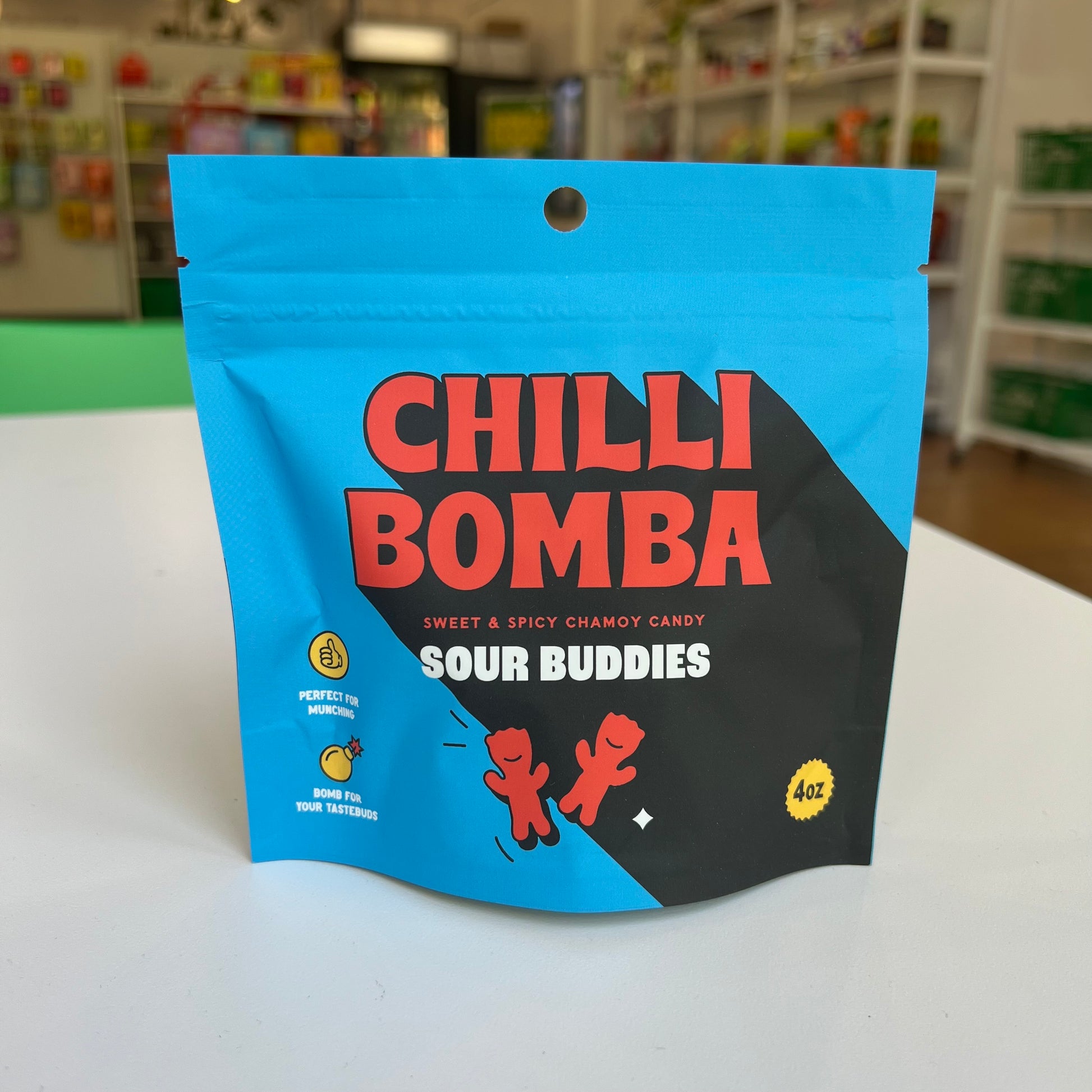 Chilli Bomba Sour Buddies candy package on a white surface in bright blue resealable pouch packaging.